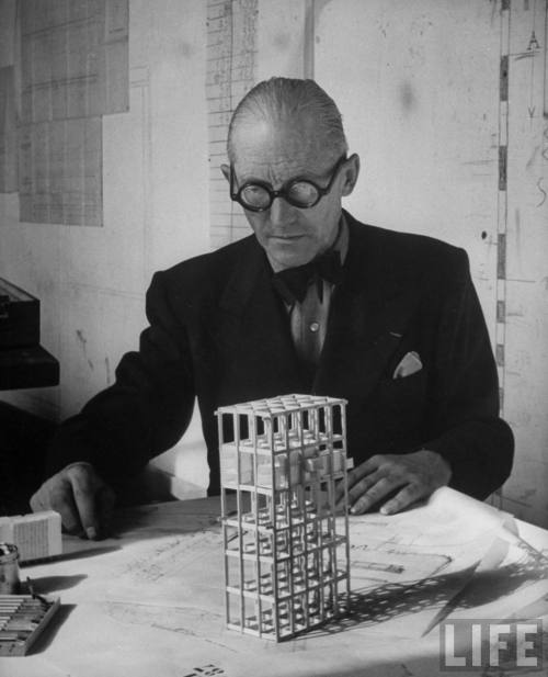 Architect Le Corbusier studying architectural plans & small model of building in his office-- Paris, France 1946.