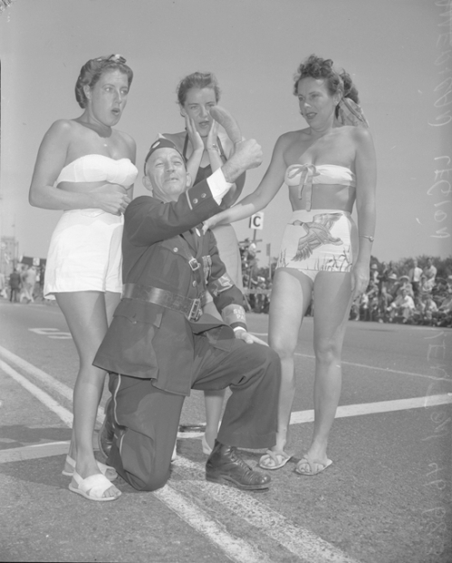 Man wearing gag thumb with three bathing beauties, Long Beach, CA  --1949.  Someone please explain...